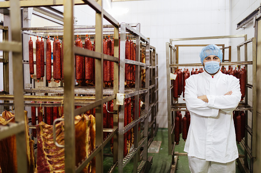 Professional butcher working at raw meet processing plant. He is checking quality of dried meet.