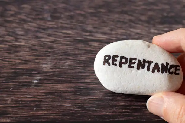 Hand-holding rock with handwritten word "repentance" over a wooden background. Top view, copy space. Christian change, confession of sin, and humility, biblical concept.