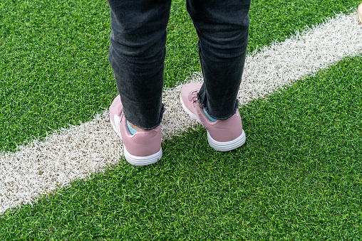 Female legs in pink sneakers standing on white line on green grass field