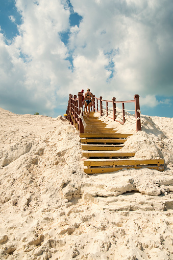Woman climbing stairs of a wooden pier on an edgy beach. Rear view. Vertical full length outdoors shot with copy space. This was taken in Cayo Largo, Cuba.