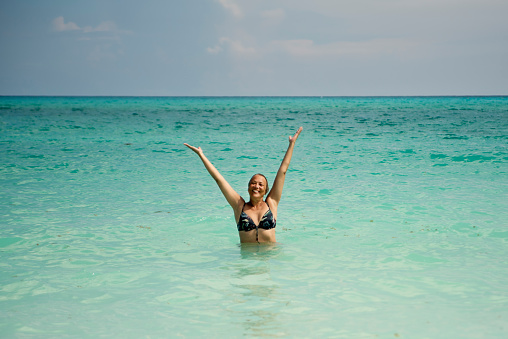 Beautiful 50+ woman enjoying being in the ocean. She is wearing a bikini and is tanned and relaxed. Horizontal full length outdoors shot with copy space. This was taken in Cayo Largo, Cuba.