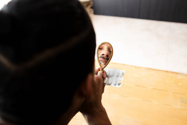 istock Latino guy looking at his broken tooth reflected in the mirror and holding his medication in his hand. 1704810446