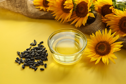 Sunflower oil, seeds and flower on yellow background.