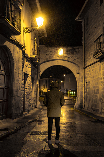 Young and unrecognizable boy walks alone at night through the streets of a town in the rain. Olite
