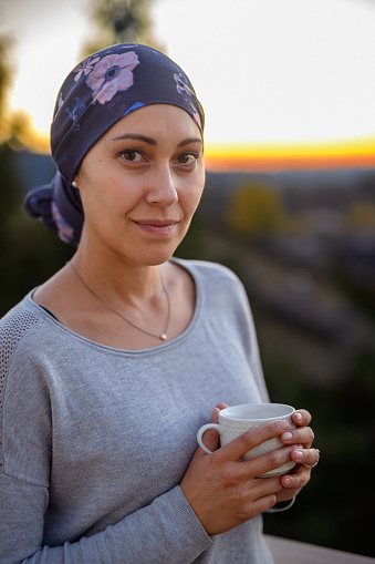 Portrait of a multiracial woman of Asian and Pacific Islander descent enjoying a cup of tea while watching the sunset from the back patio of her home. The woman if filled with hope and gratitude for the support she has received from family, friends and her medical team.
