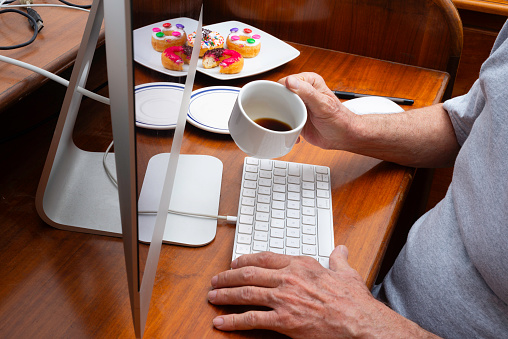 Mature man working from home with computer  with cup of black coffee and sweet doughnut .
