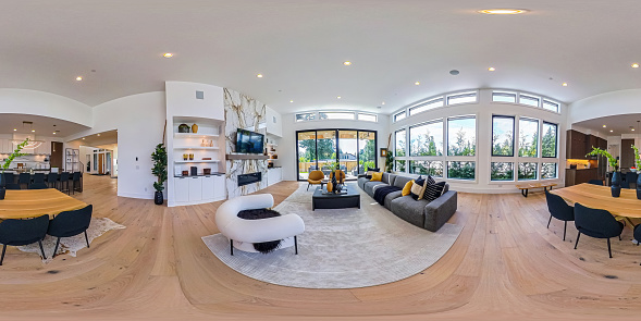 360-degree Photo of a modern luxury home interior, living room, kitchen and dining area, and entryway, surrounded by large windows that allow lots of natural light