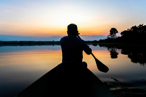 Silhouette of a native man paddling canoe at dusk calm water