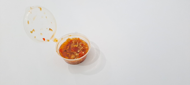 Red hot chilli pepper sauce in plastic cup isolated on a white background