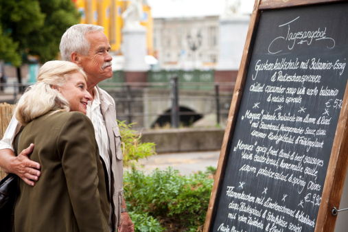 Fond senior couple is studying the menu of a restaurant on a board in an urban scene in Berlin, Germany. Selective focus on the seniors