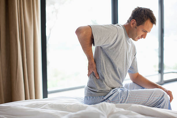 uomo con mal di schiena seduta sul letto - backache foto e immagini stock