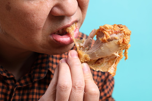 The Asian man eating deep fried chicken on the green background.