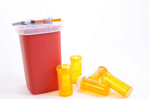 Empty medicine bottles and syringe with a disposal for sharps.  Discarded meds. 