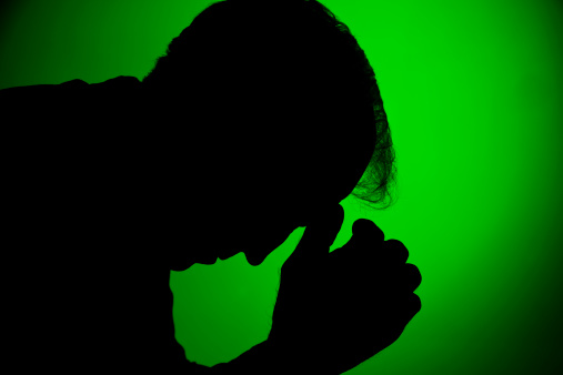 Silhouette of depressed man with head in hands against a green spot background   