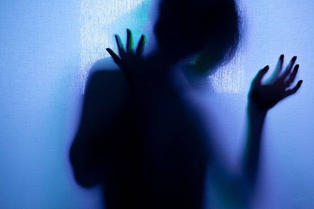 Silhouette of an emotional Woman behind a screen with raised arms.  Blue lighting.   