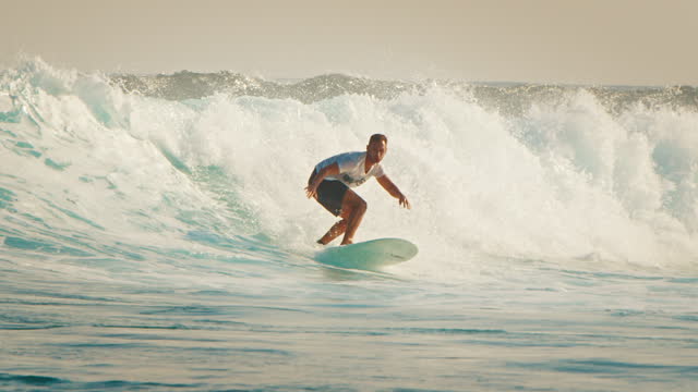 Beginner adult male surfer surfs the wave in the Maldives at sunset