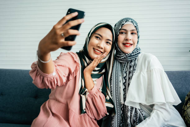 dois amigos muçulmanos com hijab tirando uma selfie - women holding shopping bag living room - fotografias e filmes do acervo