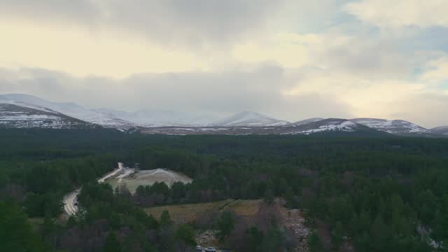 Aerial Drone Footage Showcasing a Scenic Forested Terrain with Magnificent Mountains as a Spectacular Backdrop in Scotland.