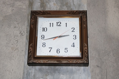 Mechanical wall clock, brown color , on a cement wall, rustic style, vintage, no people. Antique box-shaped wall clock