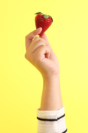 The Asian woman holding strawberry in the hand on the yellow background.