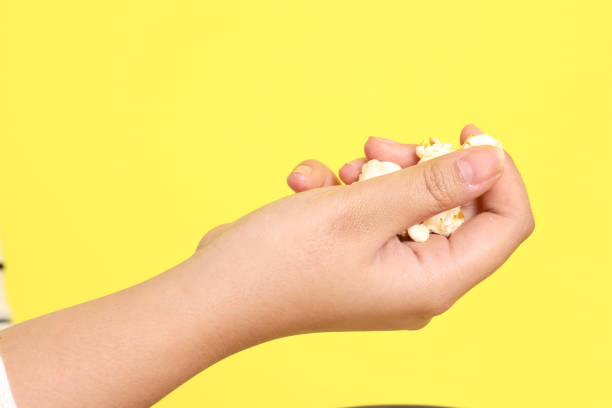 The Asian woman holding popcorn in the hand on the yellow background.