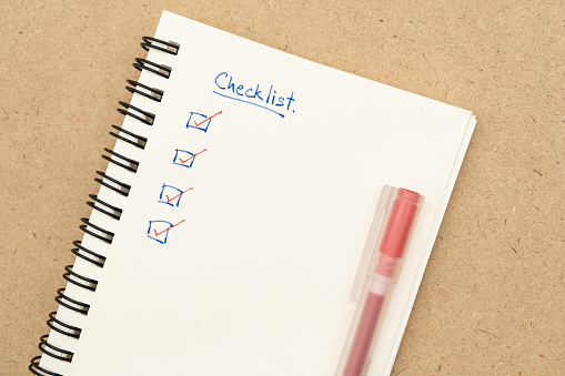 Top view of notebook with handwritten Checklist text and red pen. Checklist concept, checklist box with red checkmark. Blank checklist for text.