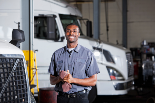 African American man (20s) in service garage repairing semi-trucks.
