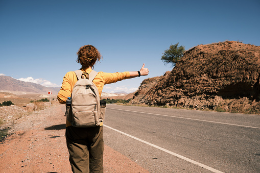 Female tourist is hitchhiking on mountain road