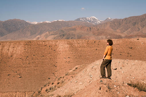 Female tourist is standing above mountain valley and looking at view
