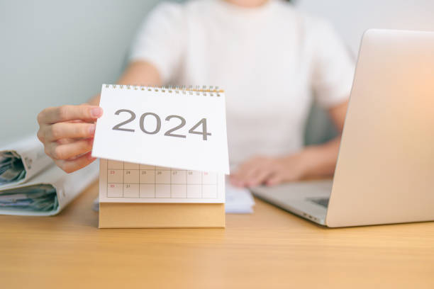 calendario del año 2024 en la mesa con una mujer de negocios usando una computadora portátil. cuenta atrás, feliz año nuevo, resolución, metas, plan, acción, misión y concepto financiero - enero fotografías e imágenes de stock