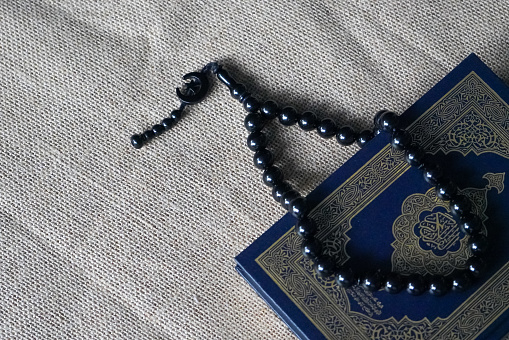 The Quran, also romanized Qur'an or Koran, is the central religious text of Islam, believed by Muslims to be a revelation from God (Allah). Black prayer beads.