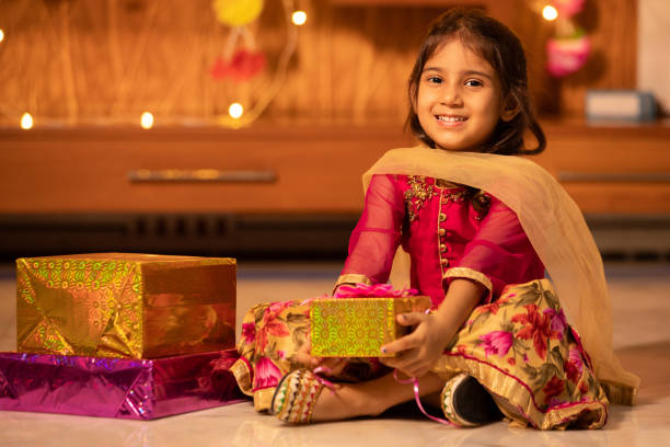 Happy little indian girl kid holding gift boxes in hand celebrating Diwali while sitting on floor, Raksha Bandhan, Bhai Dooj concept. Happy little indian girl kid holding gift boxes in hand celebrating Diwali while sitting on floor, Raksha Bandhan, Bhai Dooj concept. beautiful traditional indian girl stock pictures, royalty-free photos & images