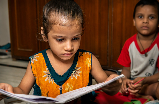 Education – Indoor portrait of rural Indian little girl studying and reading a book in the classroom.