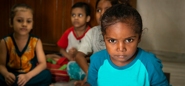 Low key indoor close-up portrait of rural Indian child staring at the camera with a blank expression.