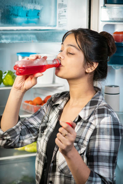 istock Woman drinking soft drink while standing front of the fridge in summers. 1705440712