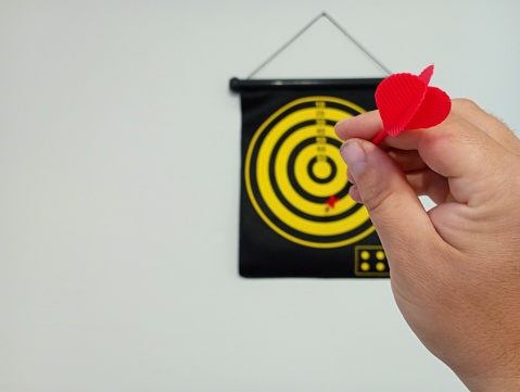 A hand throws a dart at a target hanging on the wall. Focus on dart in hand. A sports game for leisure and recreation in nature.