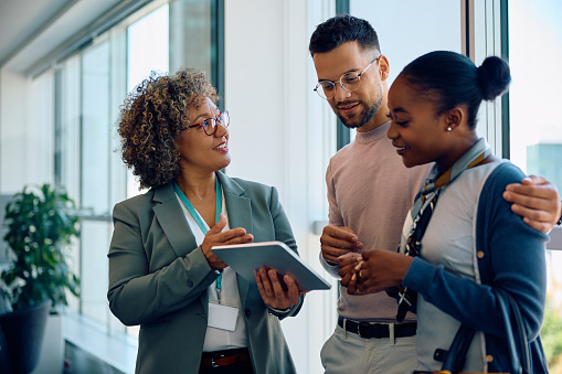 Happy multiracial couple and their financial advisor using touchpad on a meeting in the office.