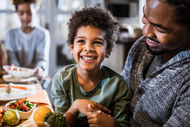 Cheerful black boy with his father at dining table.