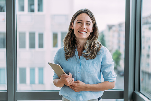 Shot of successful young businesswoman standing in the office and holding digital tablet. Portrait of a beautiful smiling businesswoman standing in her office and looking at camera.