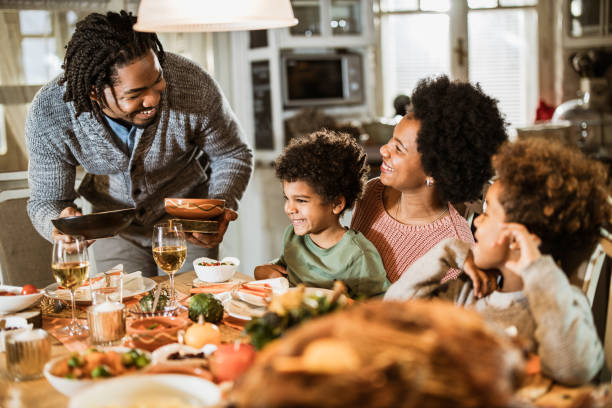 istock Happy black father serving food to his family at dining table. 1705505607
