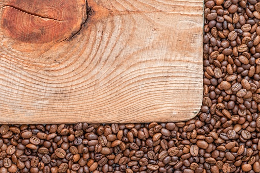 A rectangular board in the corner of a pile of coffee beans.