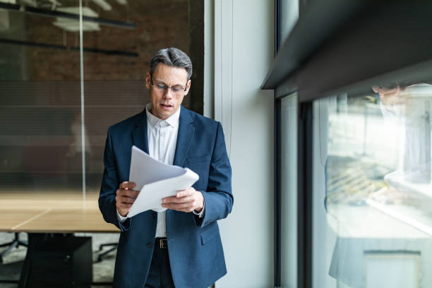 istock Mid adult businessman reading documents by the window. 1705535285