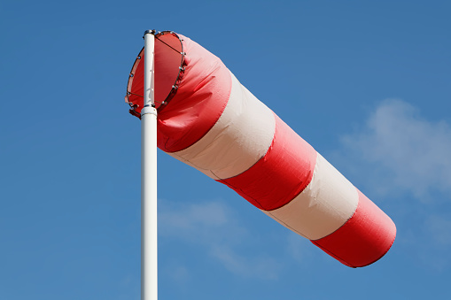 A red and white striped windsock on a pole against a blue sky.