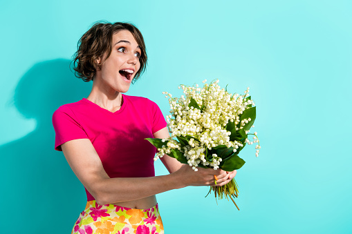 Portrait of cute astonished girl arms hold fresh flowers look empty space isolated on aquamarine color background.