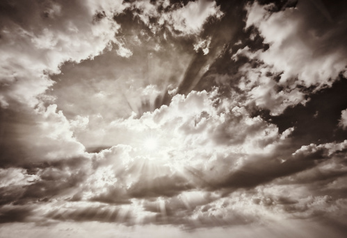 Monochrome image showing the sun creating rays of light fiiltering through clouds.