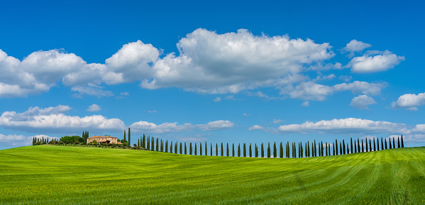 Beautiful Tuscan landscape with traditional farmhouse and dramatic clouds on a sunny day in Val d'Orcia, Italy