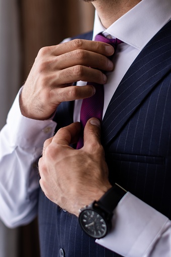 A mature adult male wearing a tailored suit and a bright purple tie, adjusting the knot