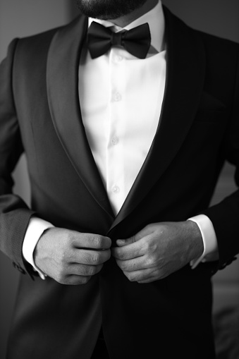 This black and white portrait features a mature man in a formal suit adjusting the buttons of his shirt