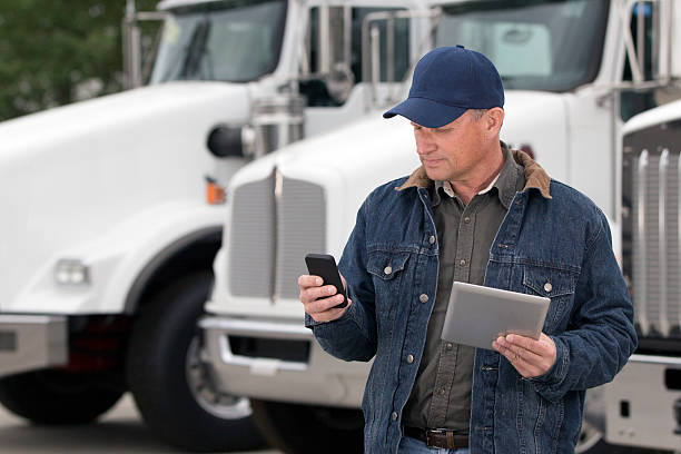 Multitasking Truck Driver A royalty free image from the trucking industry of a truck driver using a cellphone and tablet computer in front of semi trucks driver occupation photos stock pictures, royalty-free photos & images