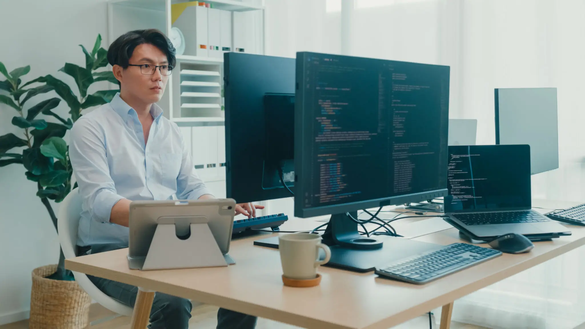 Young Asian man software developers using computer to write code sitting at desk with multiple screens work at office. Programmer development.
